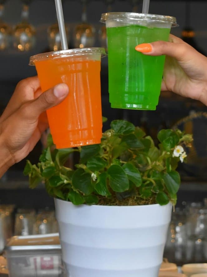 Two friends clinking orange and green slushies